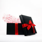 A black gift box with a red ribbon is partially open, revealing white tissue paper with red snowflake patterns against a white background.