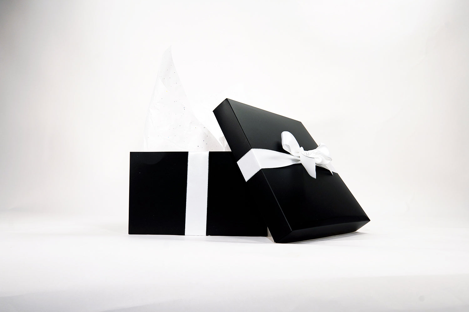 A black gift box with a white ribbon is partially open, showing white tissue paper. The box is set against a plain white background.