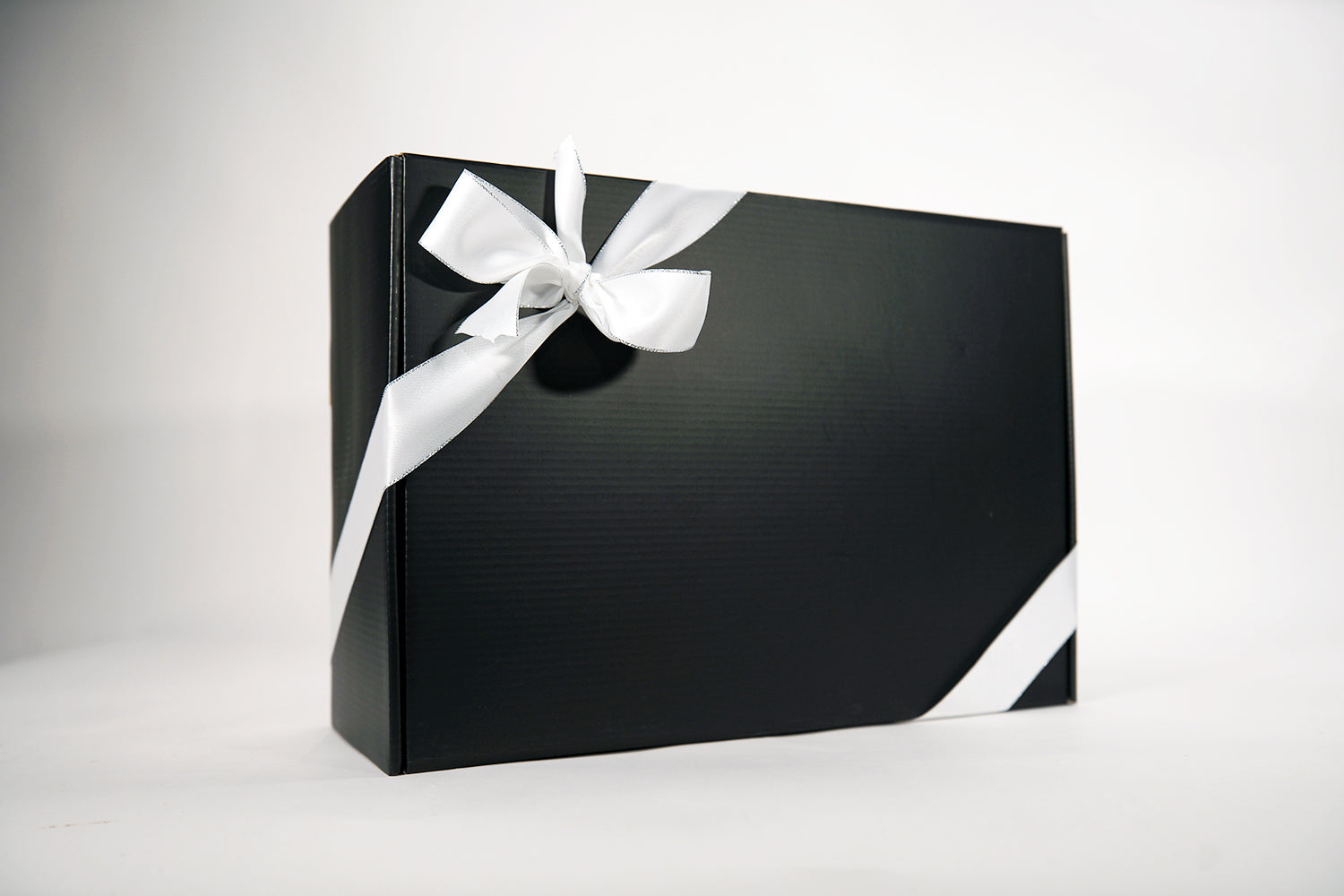A sleek black gift box wrapped with a smooth white ribbon tied in a bow sits against a plain white background.