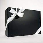 A sleek black gift box wrapped with a smooth white ribbon tied in a bow sits against a plain white background.