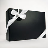 A sleek black gift box wrapped with a smooth white ribbon tied in a bow sits against a plain white background.