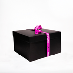 A large black gift box wrapped with a purple ribbon that has the words "Prospector Popcorn" printed on it. The box is set against a plain white background.