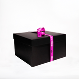 A large black gift box wrapped with a purple ribbon that has the words "Prospector Popcorn" printed on it. The box is set against a plain white background.