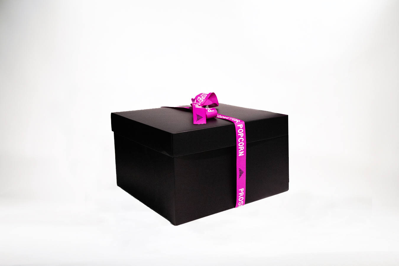 A large black gift box wrapped with a purple ribbon that has the words "Prospector Popcorn" printed on it. The box is set against a plain white background.