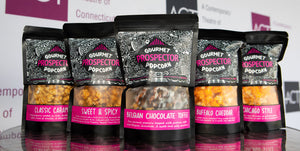 Five bags of prospector popcorn are lined up on a table at a corporate event