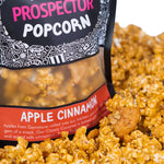 A bag of Apple Cinnamon Prospector gourmet popcorn  sits in a pile of its own popcorn.