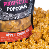 A bag of Apple Cinnamon Prospector gourmet popcorn  sits in a pile of its own popcorn.