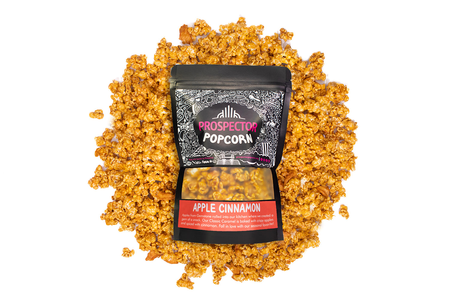 A bag of Apple Cinnamon Prospector gourmet popcorn lays on a bed of its own popcorn