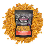 A bag of Apple Cinnamon Prospector gourmet popcorn lays on a bed of its own popcorn