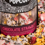 A bag of Chocolate Strawberry gourmet popcorn sits in a pile of its own popcorn