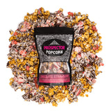 A bag of Chocolate Strawberry gourmet popcorn lays on a pile of its own popcorn.