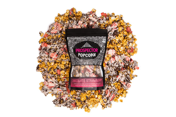 A bag of Chocolate Strawberry gourmet popcorn lays on a pile of its own popcorn.