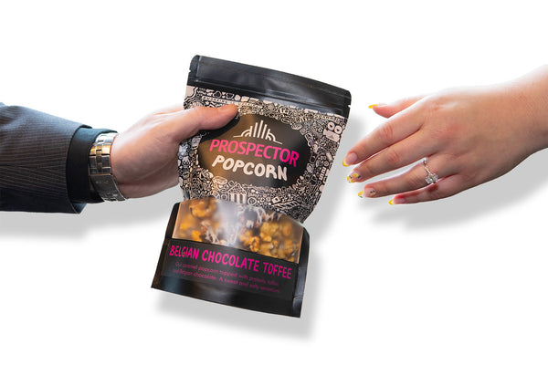 One hand giving a bag of gourmet popcorn Belgian chocolate toffee to another hand as a corporate gift. 