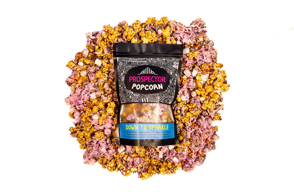 A bag of Down to Sparkle gourmet popcorn lays on a bed of its own popcorn.