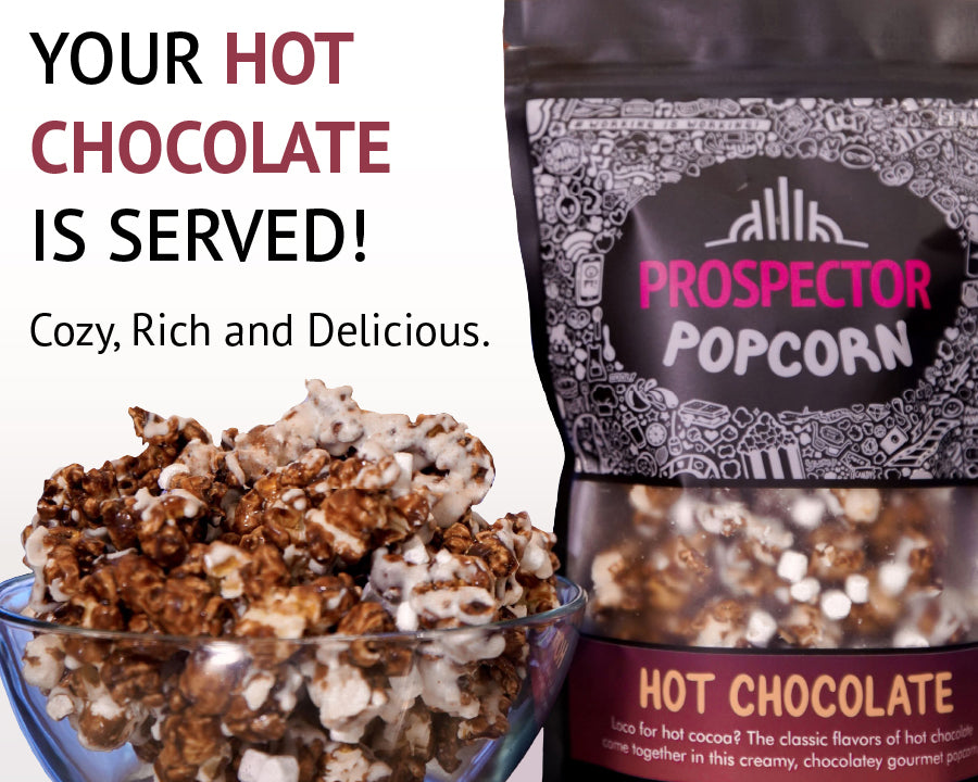 A clear bowl filled with chocolate-coated popcorn is in the foreground. Behind it is a bag labeled "Prospector Popcorn" with "Hot Chocolate" flavor indicated. The text reads "Your Hot Chocolate is Served! Cozy, Rich and Delicious.