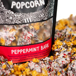 A bag of Peppermint Bark gourmet Prospector Popcorn stands in a pile of its own popcorn.