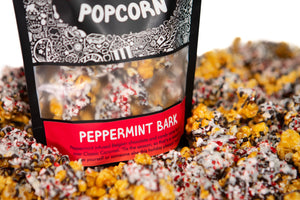 A bag of Peppermint Bark gourmet Prospector Popcorn stands in a pile of its own popcorn.