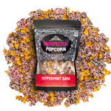 A bag of Peppermint Bark gourmet Prospector Popcorn lays on a pile of its own popcorn.