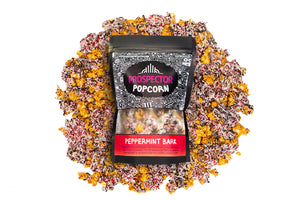 A bag of Peppermint Bark gourmet Prospector Popcorn lays on a pile of its own popcorn.
