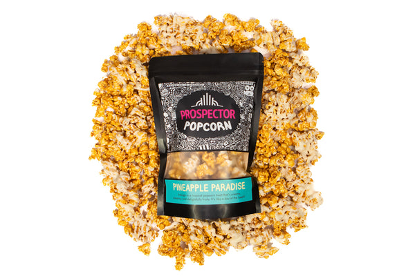 A bag of Pineapple Paradise popcorn lays on a pile of its popcorn.