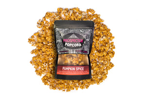 A bag of Pumpkin Spice gourmet popcorn lays on a pile of popcorn on a white background.