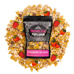 A bag of Strawberry Ice Cream Gourmet Popcorn lays on a pile of its popcorn. 4 strawberries lay on the pile around the bag.