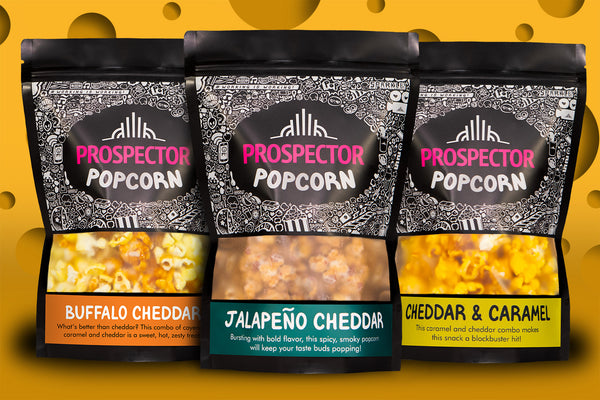 3 bags of gourmet popcron from prospector popcorn in front of a yellow background that looks like swiss cheese