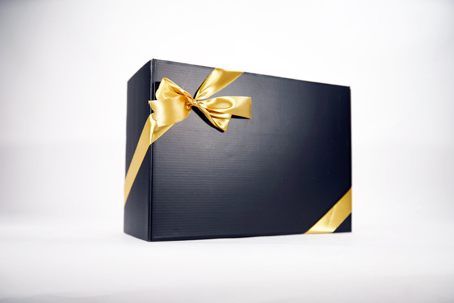 A matte black gift box adorned with a shiny gold ribbon and bow sits against a plain white background. The box exudes an elegant and luxurious appearance.