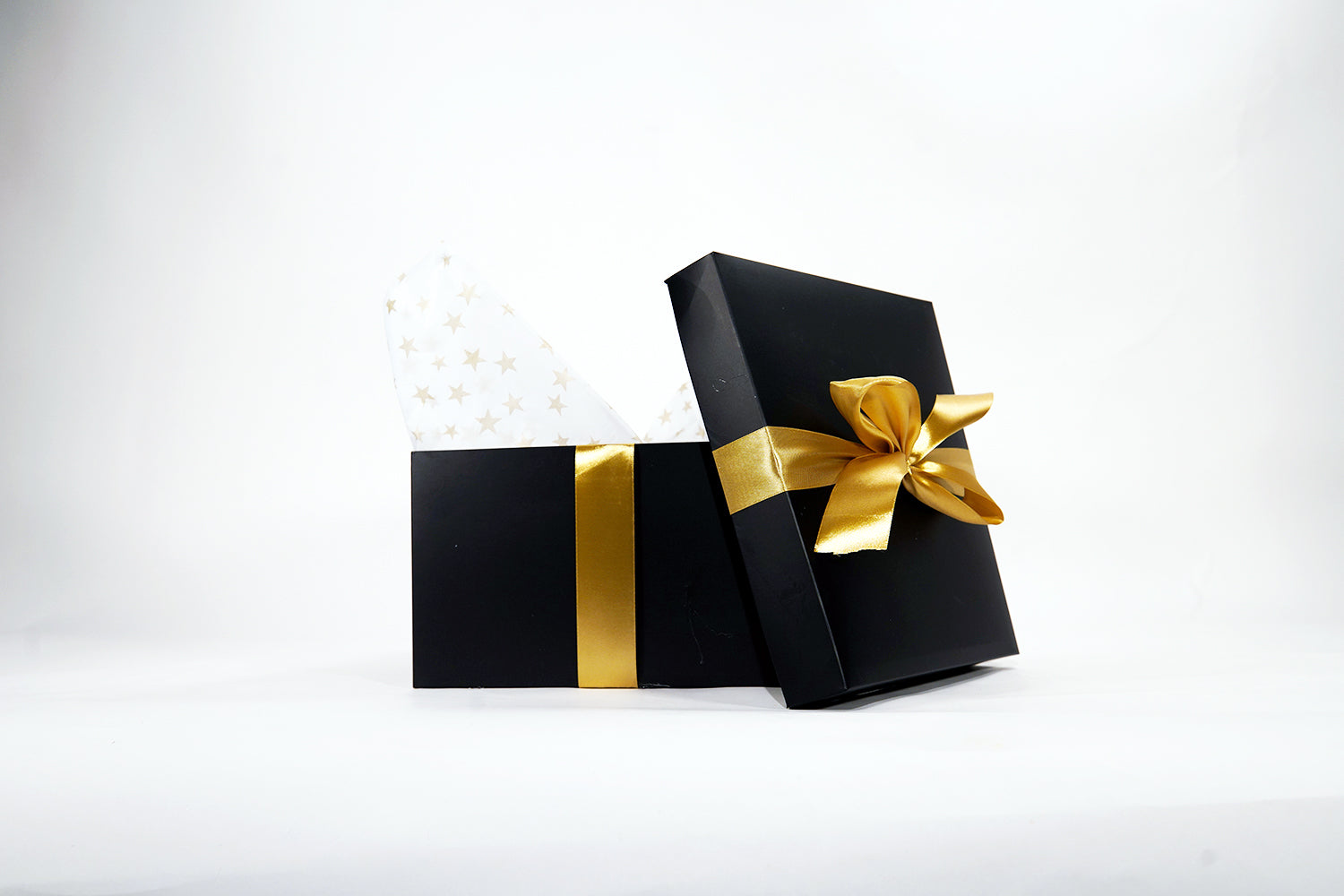 An open black gift box with a gold ribbon and bow, revealing white tissue paper with gold stars. The background is plain white.