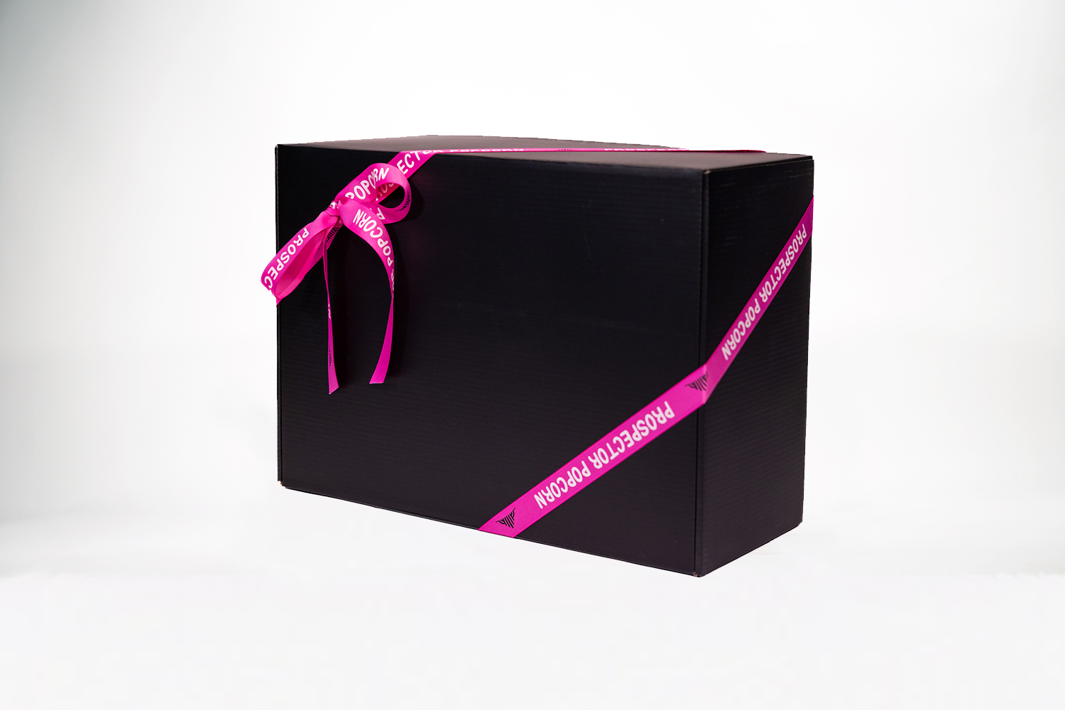 A large black gift box wrapped with a purple ribbon that has the words "Prospector Popcorn" printed on it. The box is set against a plain white background.