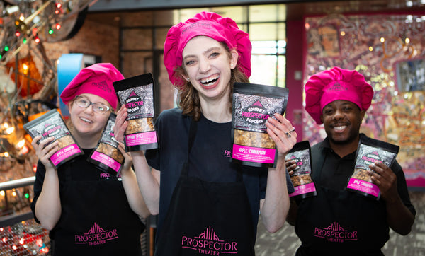 Three Prospects hold up bags of Gourmet Popcorn while wearing pink chefs hats and black aprons