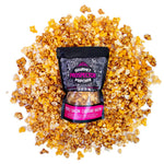 A bag of Maple Bacon Cheddar Bacon Gourmet Popcorn lays on a pile of its own popcorn on a white background