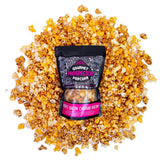 A bag of Maple Bacon Cheddar Bacon Gourmet Popcorn lays on a pile of its own popcorn on a white background