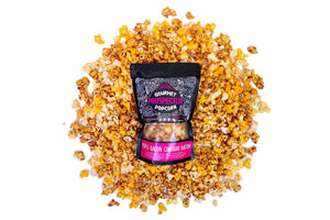 A bag of Maple Bacon Cheddar Bacon Gourmet Popcorn lays on a pile of its own popcorn on a white background