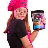 Popcorn Chef, Brooklyn, holds a bag of Down to Sparkle gourmet popcorn as she wears a pink apron and pink chefs hat.