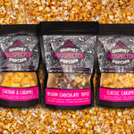 Cheddar and Caramel, Belgian Chocolate Toffee, and Classic Caramel gourmet popcorn bags lay on a bed of popcorn