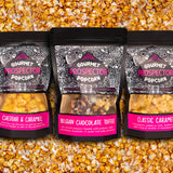 Cheddar and Caramel, Belgian Chocolate Toffee, and Classic Caramel gourmet popcorn bags lay on a bed of popcorn