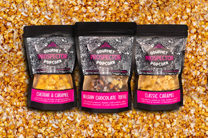 Cheddar and Caramel, Belgian Chocolate Toffee, and Classic Caramel gourmet popcorn bags lay on a bed of popcorn